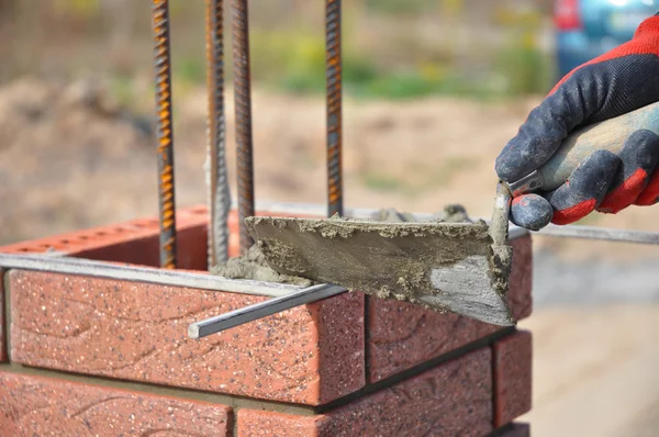 Bricklayingen närbild. Muraren hand håller en spackel och bygga en tegel staket kolumn. — Stockfoto