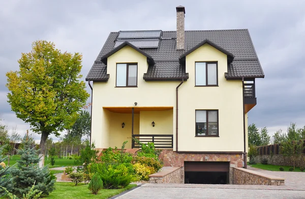 Maison moderne avec puits de lumière, chauffage solaire par panneau d'eau, lucarnes, toit carrelé, gouttière, clôture, fenêtres de toit de garage, protection du toit contre la cheminée à neige, beau jardin paysager. Belle maison extérieure — Photo