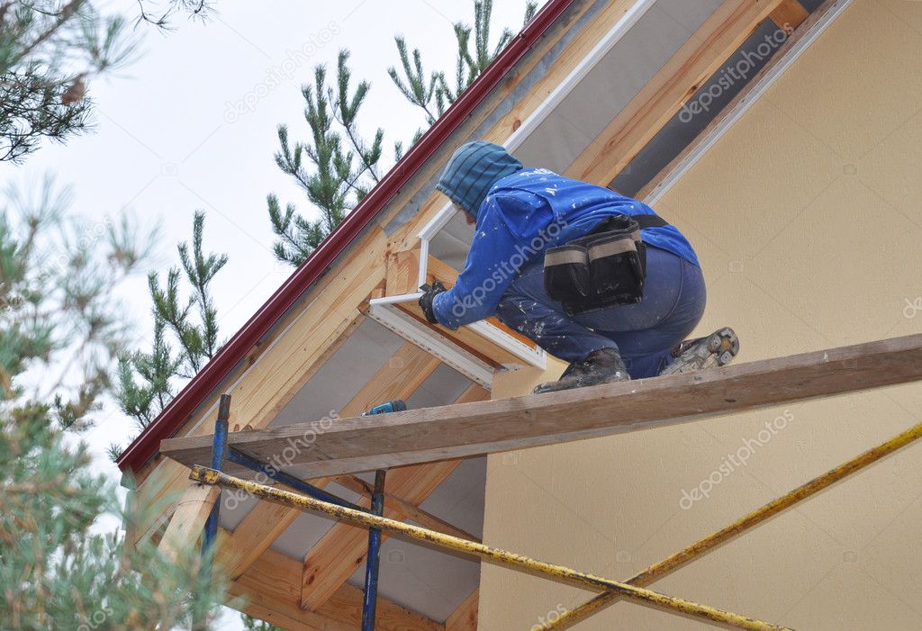 Roofer on the Corner of House  Install Soffit. Roofing Construction. Soffit is Usually Constructed of Vinyl, Wood or Aluminum and is Installed on the Underside of Roof Overhangs 