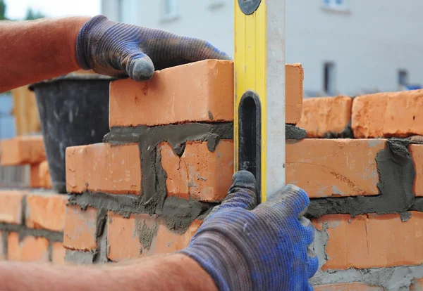 Briqueteuse utilisant un niveau d'esprit pour vérifier le nouveau mur de briques rouges Ou — Photo