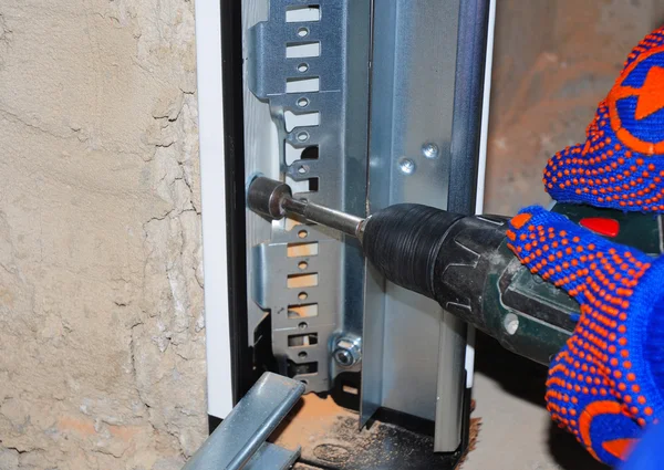 Instalación del panel de puerta de garaje. Hombre usando taladro para conectar la puerta de plástico y el panel de perfil de metal a la pared . —  Fotos de Stock