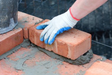 İnşaat işçisi havan topu ile kırmızı tuğla döşüyordu.