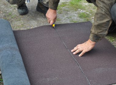 Roofer  cutting roll roofing felt or bitumen during waterproofin