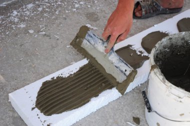 Man's Hand Plastering a Wall Styrofoam or Foam Board Insulation with Trowel. clipart