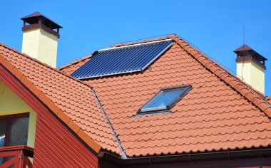 Enerji verimliliği kavramı. Kırmızı Isıtma güneş enerjili su paneli closeup evin çatı Yıldırımdan korunma, ışıklıklar, baca ve çatı penceresi ile döşeli