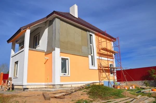 Construction or repair of the rural house with balcony, eaves, windows, chimney, roofing, fixing facade, insulation, plastering and using color. Stock Photo