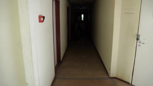 Hombre con gorra mochila caminar por pasillo oscuro bajar escaleras de madera dentro del edificio — Vídeo de stock