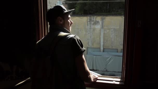 Back side of man in cap watch in window. Inside building. Day. Bright sun — Stock Video