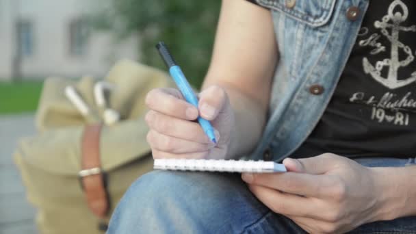 Man handen verf iets door blauwe marker op papieren notitieblok. Straat. Zomerdag — Stockvideo