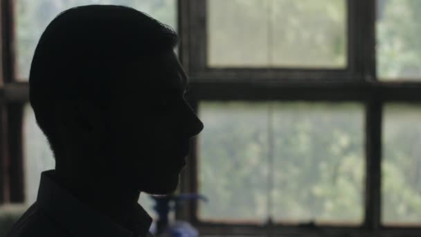 Silhouette of man head strat smoking a cigarette. Indoor. Window on background — Stock Video