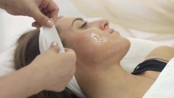 Gros plan de mains de cosmétologue faire épilation des joues de fille dans le salon de beauté . — Video