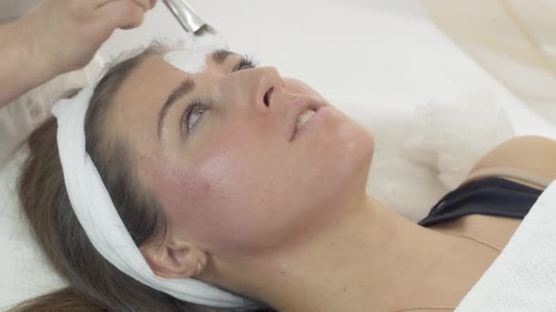 Close up de mãos cosmetologist colocar máscara branca na menina no salão de beleza . — Vídeo de Stock