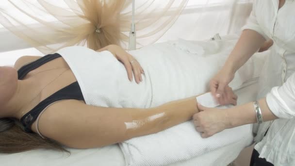 Cosmetologist adulto epilate menina mão por tira de cera no salão de beleza. Tiro médio — Vídeo de Stock