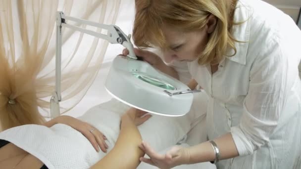 Cosmetólogo examina mano de niña en lupa en salón de belleza. Tiro medio — Vídeos de Stock