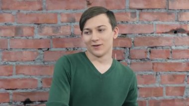 Yeşil kazak içtenlikle gülümseyen genç adam. Tuğla duvar arka plan. Seçmeler