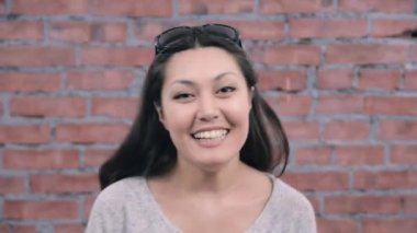 Siyah uzun saçları yetişkin kız memnuniyetle kamera konuş. Döküm. Tuğla duvar