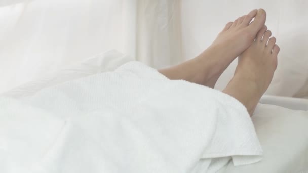 Женские ноги и тело под белым одеялом в салоне красоты. Девушка на процедуры — стоковое видео