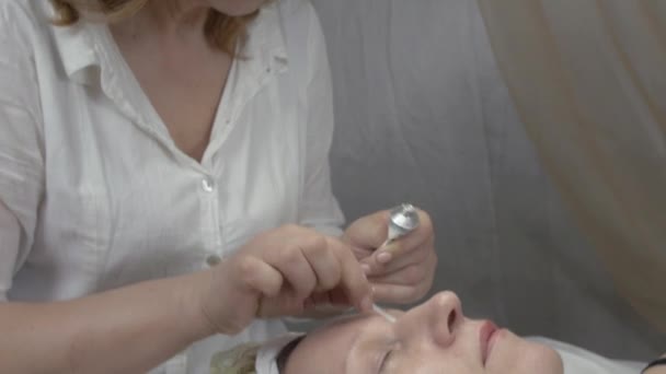 Cosmetólogo mirar en lupa, poner gel bajo los ojos de la mujer en salón de belleza . — Vídeos de Stock