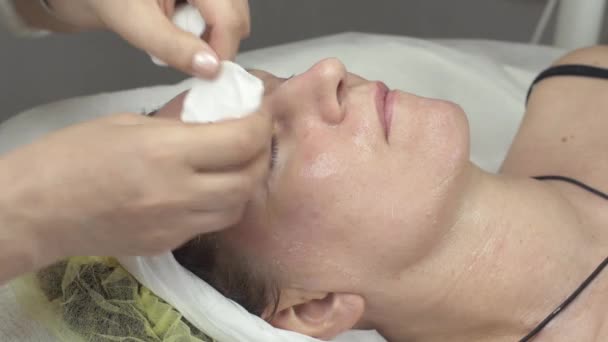 Cosmetologist pôs a almofada de algodão, cheesecloth na cara de mulher adulta no salão de beleza . — Vídeo de Stock