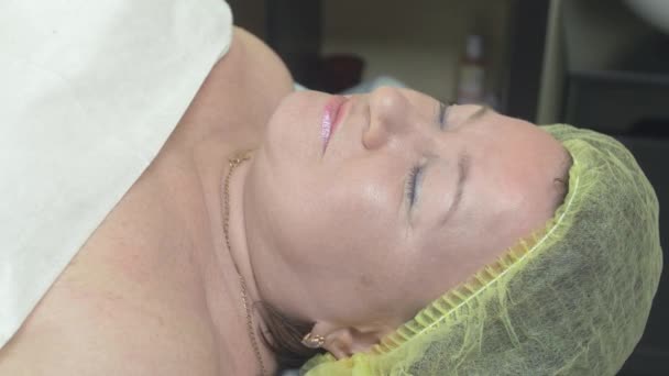 Обличчя дорослої товстої жінки лежить в салоні краси на процедурах. Макіяж. Посмішка — стокове відео