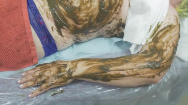 Cosmetologist put seaweed mixture on fat woman stomach, left hand. Spa wrapping — Stock Video