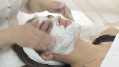 Yakın cosmetologist eller güzellik salonda kız yüzüne kil maskesi ovmak