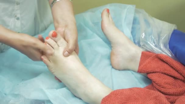 A massagista faz a massagem do pé esquerdo à mulher adulta no salão. Unhas vermelhas. Terapia — Vídeo de Stock