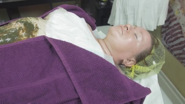 Жирная взрослая женщина лежит в салоне красоты, покрытая термопленкой. Обертка водорослей — стоковое видео