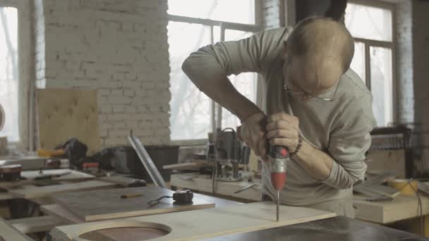 Carpintero profesional envejecido hacer agujeros en tablero de madera pulida por taladro . — Vídeo de stock