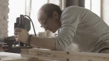 Woodworker file away edge of wooden board by plunge router. Manufacturer