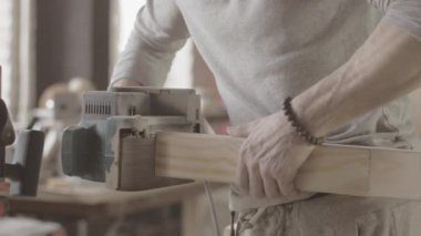Woodworker treats edge of wooden board by belt sander. Manufacturer
