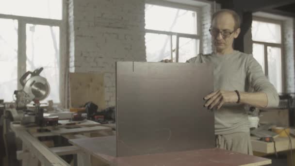 プロの大人の大工は働くテーブルの2つの等しい木製の板を接続する. — ストック動画