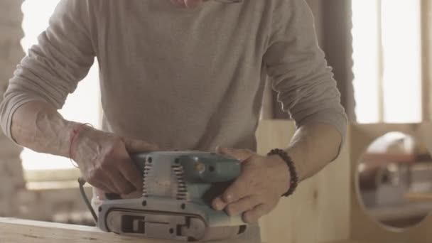 Vieilli menuisier processus minutieux planche en bois par ponceuse de ceinture. Fabricant 