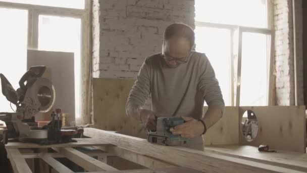 Woodworker em óculos tratar placa de madeira por lixadeira cinto. Fabricante — Vídeo de Stock