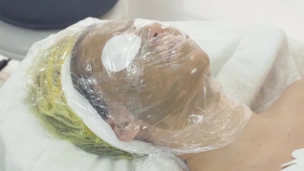 Cara de mujer cubierta por termofilm en salón de belleza. Máscara de calentamiento. Cáscara — Vídeos de Stock