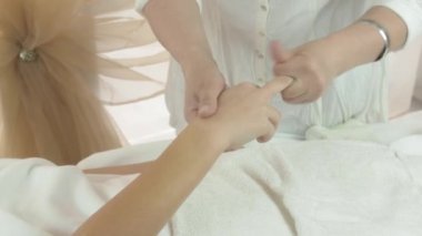 Masseuse make massage of every finger on right woman hand in beauty saloon.