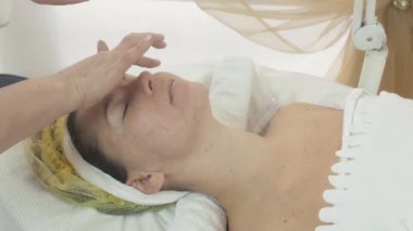 Güzellik salonda kadın yüzünde kozmetolojist yayma bit nemlendirici yağ.