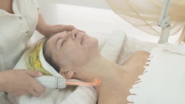 Kozmetolojist güzellik salonda kadın yüz ve boyun darsonvalizasyon yapmak.