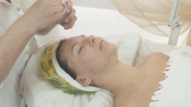 Kozmetolojist güzellik salonda kadın yüzüne yeşil kil maske koymak. Skincare