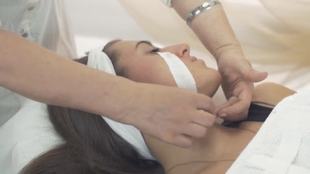 Косметолог удаляет восковую полоску с щек молодой девушки в салоне красоты . — стоковое видео