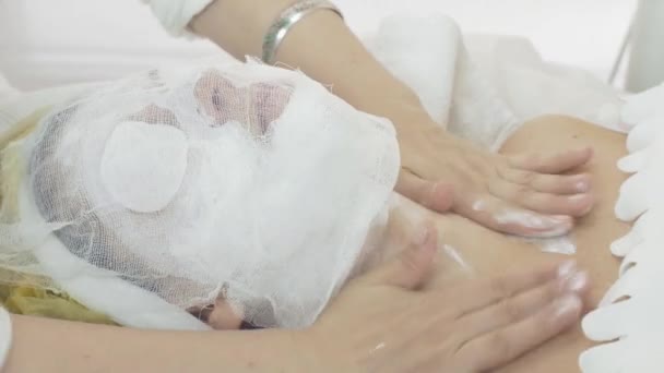 Nő arcát agyagos maszk hatálya a szépségszalon cheesecloth. Kozmetikus — Stock videók