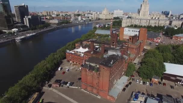 Quadrocopter latać wokół starych ceglanych budynków z rurami w mieście nad rzeką. Słoneczny letni dzień. Gród — Wideo stockowe