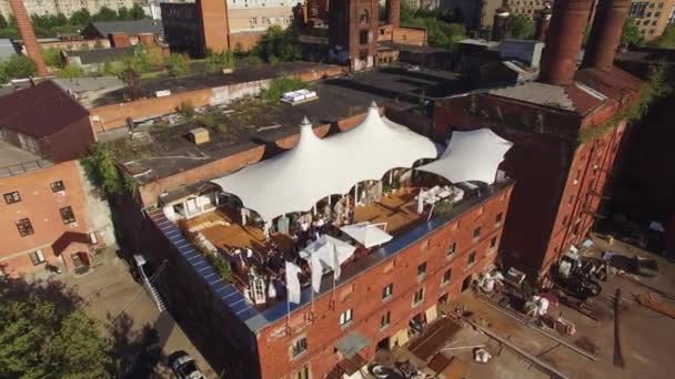 Quadrocopter знімає літній ресторан з білим наметом на даху цегляної будівлі. Сонячно. Люди. Дворик — стокове відео