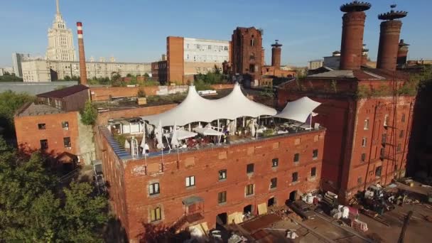 Quadrocopter voar sobre restaurante de verão com tendas brancas no telhado do edifício velho. Dia ensolarado. Pessoas — Vídeo de Stock