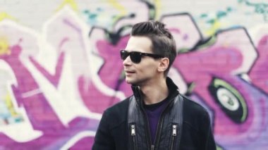 Güneş gözlüklü adam kamera jest yapmak. Şarkıcı. Graffiti arka plan üzerinde renkli duvar. Alt kültür