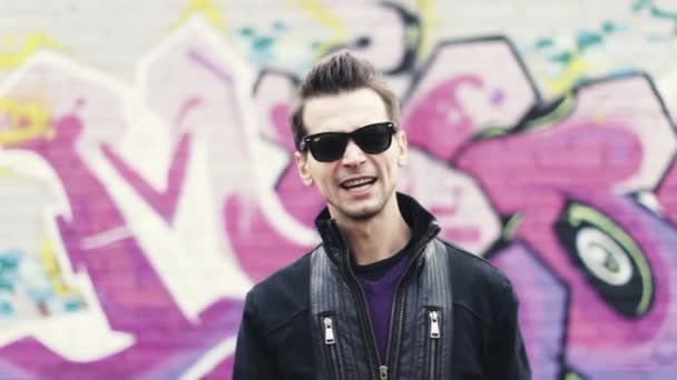 Mann mit Sonnenbrille macht Hip-Hop-Geste in Kamera. Rapper. Graffiti bunte Wand auf Hintergrund. — Stockvideo