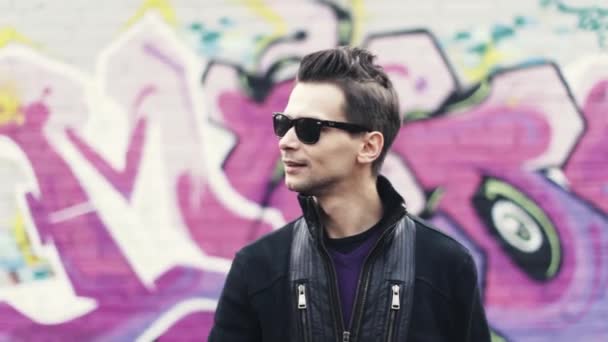 Mann mit Sonnenbrille macht Geste in Kamera. Sänger. Graffiti bunte Wand auf Hintergrund. Subkultur — Stockvideo