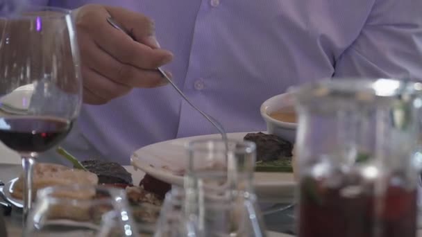 Мужчина в рубашке положил кусок тарелки с одной тарелки на другую. Столик накрыт. Стакан вина. Ужин — стоковое видео