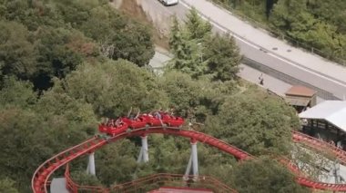 İnsanlar eğlence parkı olan kırmızı lunapark trenine binmek. Aşırı. Sevinçlilik. Yaz günü. Yeşil ağaçlar