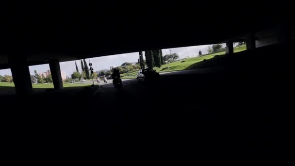 Vooraanzicht mensen rijden op de motorfiets onder brug in de stad. Veel groen. Zonnige zomerdag. — Stockvideo